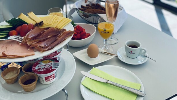 A breakfast table with various food items, a glass of orange juice, a cup of coffee, and a view of the outdoors. - Landhotel Zerlaut (Kisslegg)