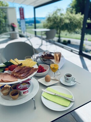 A breakfast table with various food items, a glass of orange juice, a cup of coffee, and a view of the outdoors. - Landhotel Zerlaut (Kisslegg)