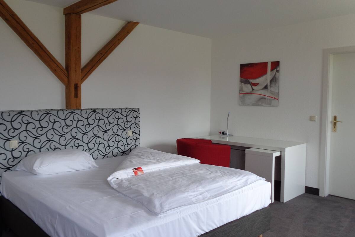 A hotel room with a bed, a desk, and a red chair.