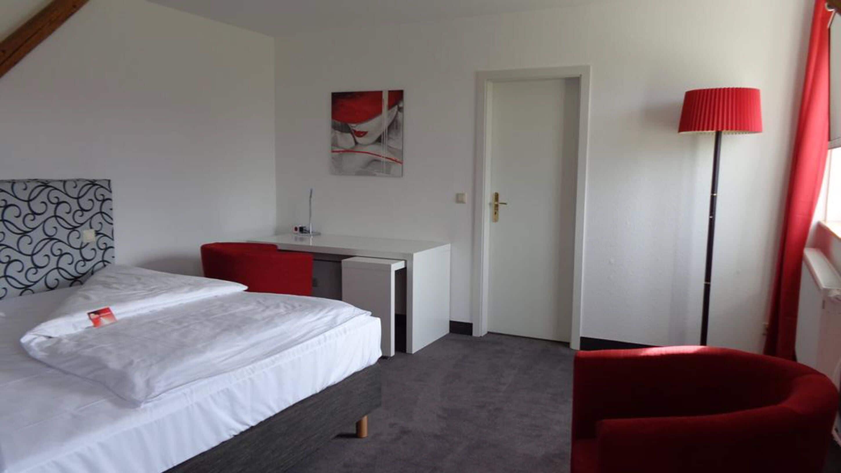 Hotellihuone, jossa on sänky, työpöytä, tuoli ja punainen lamppu.