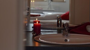 A bathroom with a mirror, a sink, a red candle, and a towel rack. - Landhotel Zerlaut (Kisslegg)