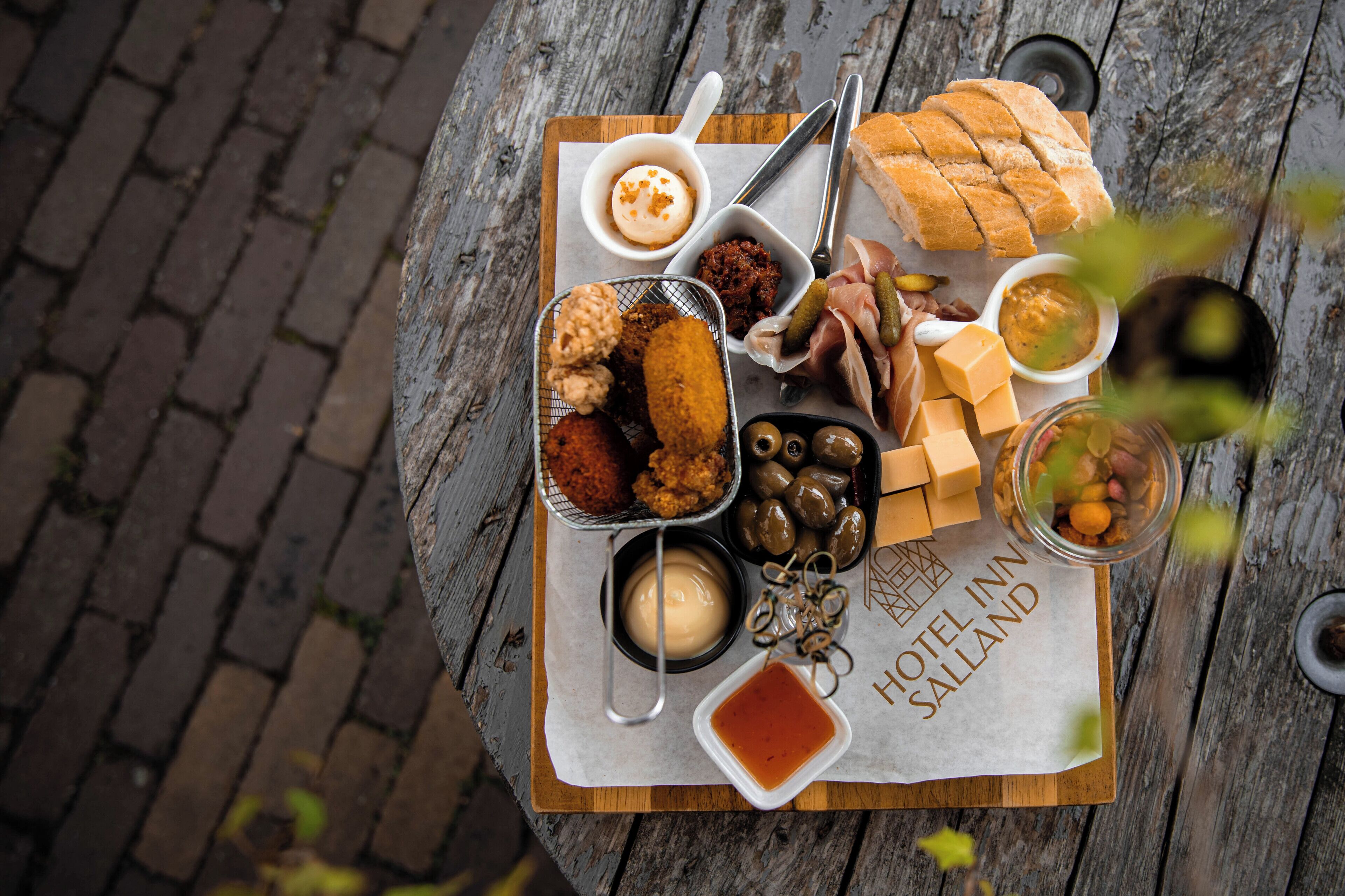 A wooden table with a variety of food items including bread, olives, and dips, placed on a sign that reads "HOTEL IN SALLAND".