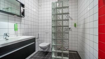 Een badkamer met een witte betegelde wand, een vloer van zwarte tegels, een wit toilet, een glazen douchecabine, een wit wastafelmeubel met een zwart aanrechtblad, en een spiegel boven de wastafel.