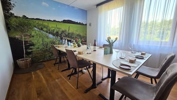 A dining area with a table set for four, chairs, a painting of a landscape, and a window with curtains.