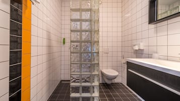 Een moderne badkamer met witte betegelde wanden, een douchecabine met glazen wanden, een vloer van zwarte tegels en een wit toilet.