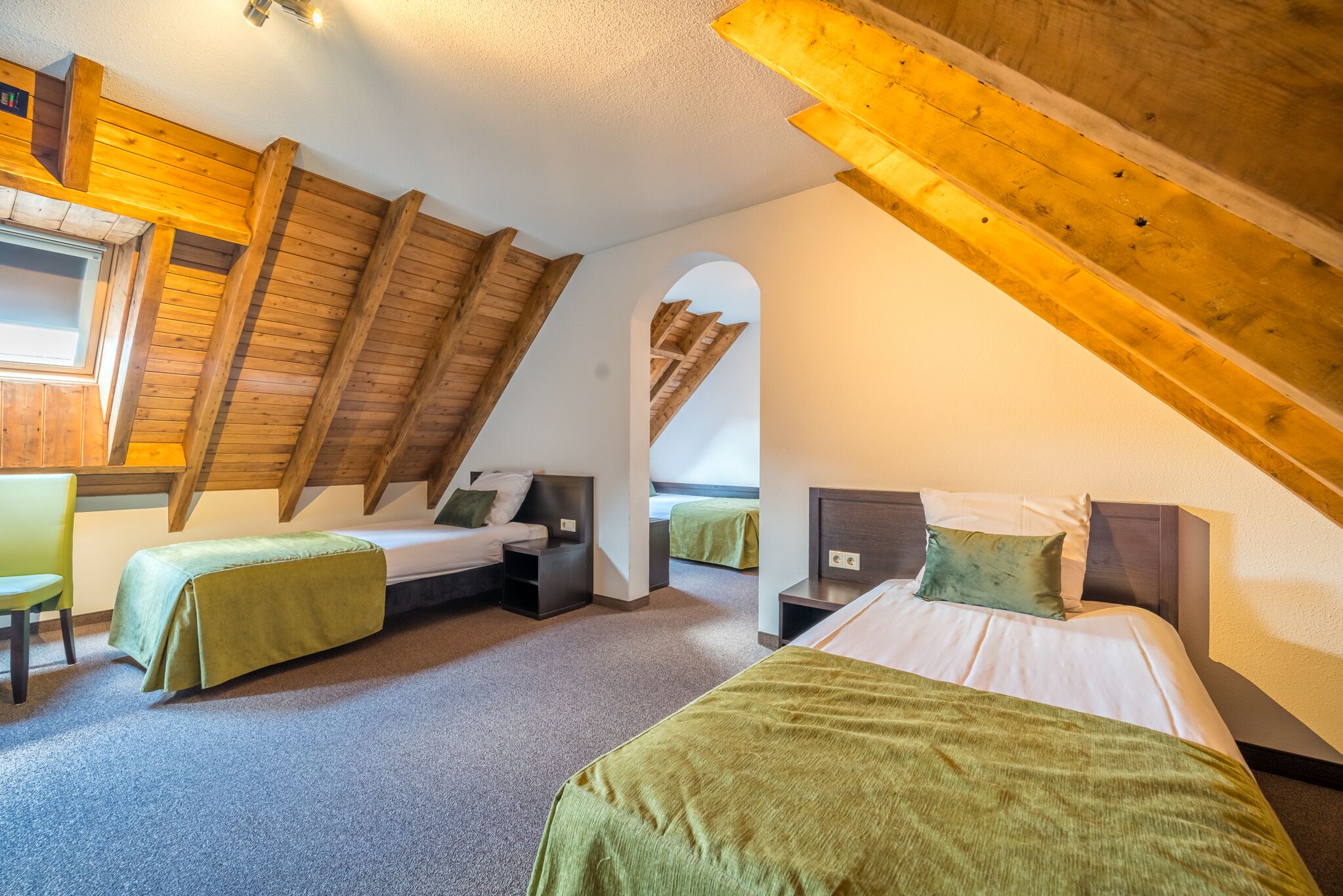 Una habitación con dos camas, vigas de madera, un tragaluz y un pequeño rincón de descanso.