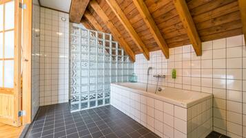 Een badkamer met een badkuip, houten balken in het plafond en een betegelde vloer.