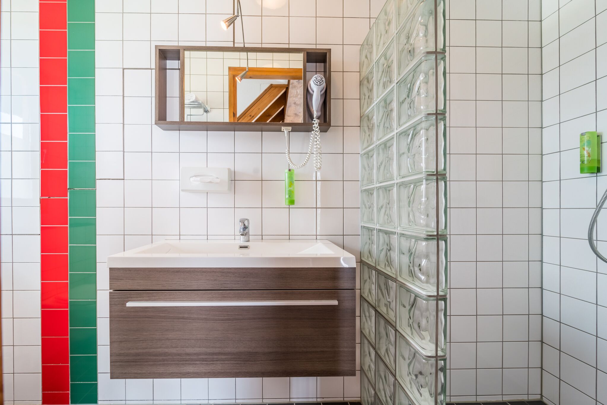 Un baño moderno con un lavabo blanco, un espejo y un secador de pelo montado en la pared.