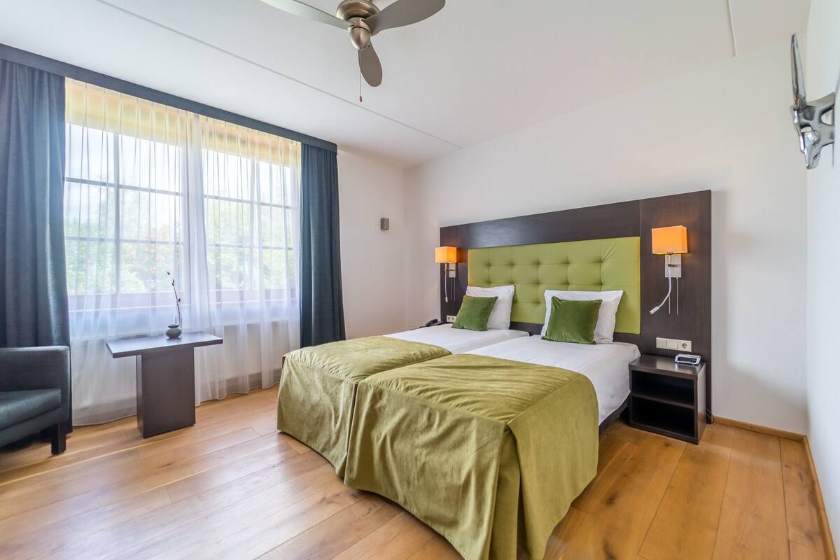 A hotel room with a bed, bedside lamps, a nightstand, a desk, and a chair.