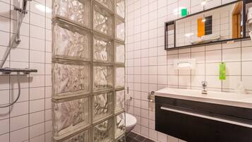 A bathroom with a glass shower enclosure, a white toilet, a black sink with a mirror above it, and a tiled wall with a grid pattern.