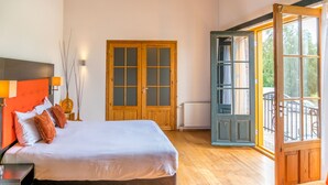 A bedroom with a large bed, wooden floor, a wardrobe, and a window with an open door. - Hotel Inn Salland (Raalte)
