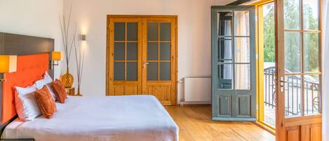 A bedroom with a large bed, wooden floor, a wardrobe, and a window with an open door.