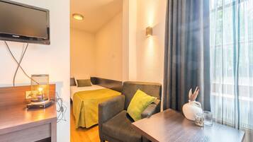 A hotel room with a bed, a chair, a desk with a lamp, a TV, and a window with curtains.