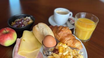 Ein Frühstücksteller mit Schinken, Käse, Eiern und einem Croissant auf einer Holztischplatte.