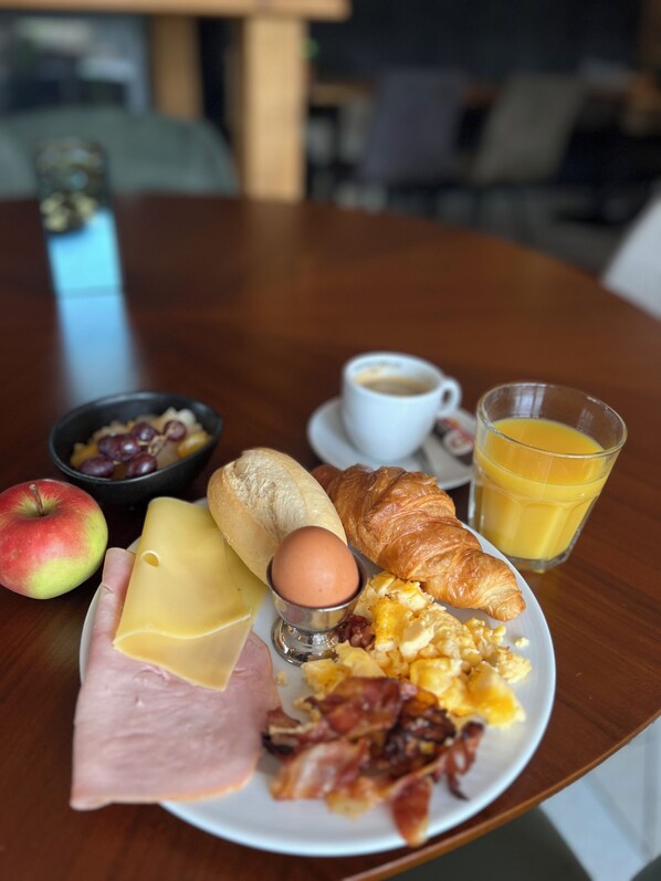 A breakfast plate with ham, cheese, eggs, and a croissant on a wooden table.