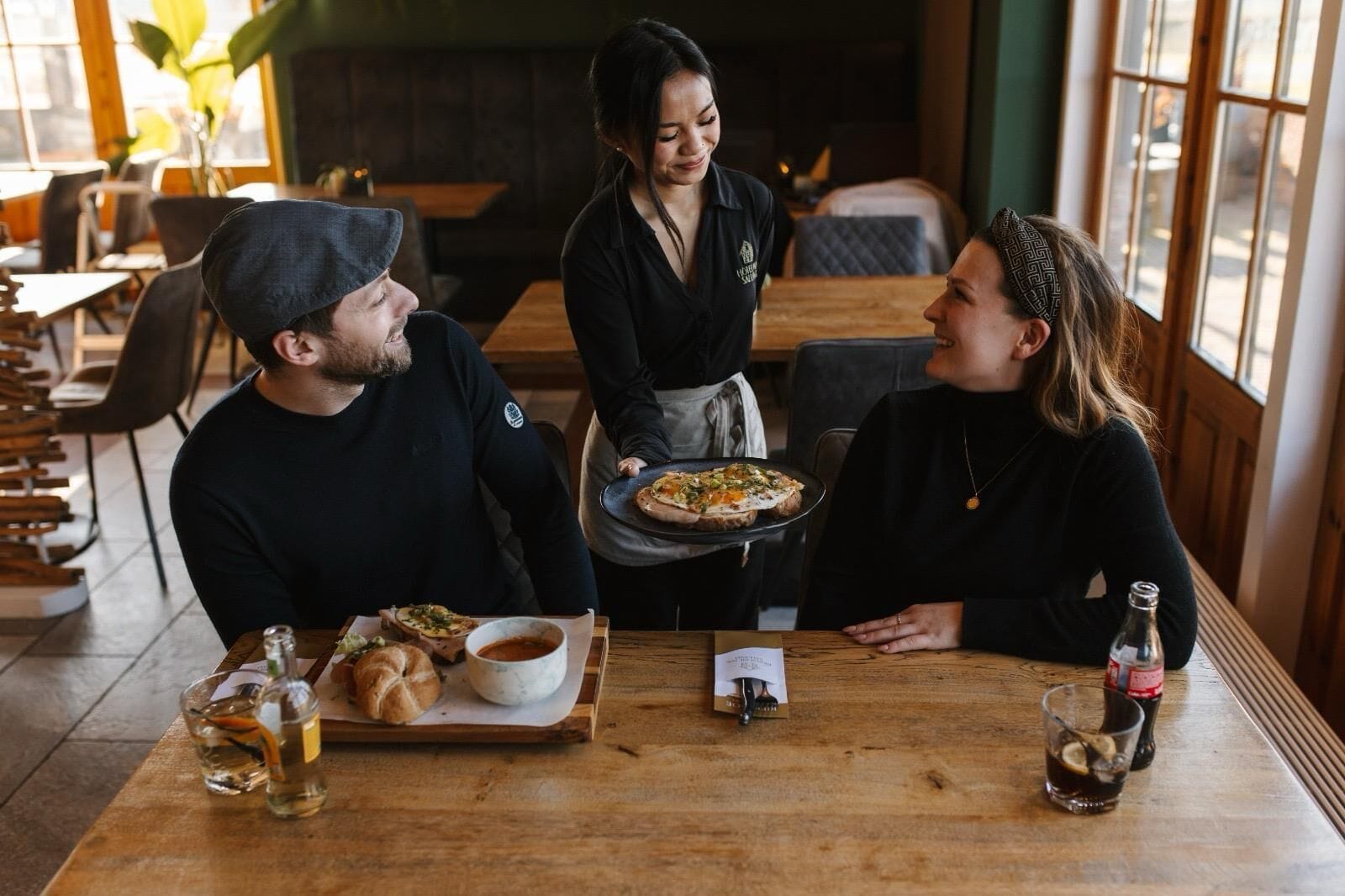 Un restaurante con mesas de madera, un camarero sirviendo comida y una carta sobre la mesa.