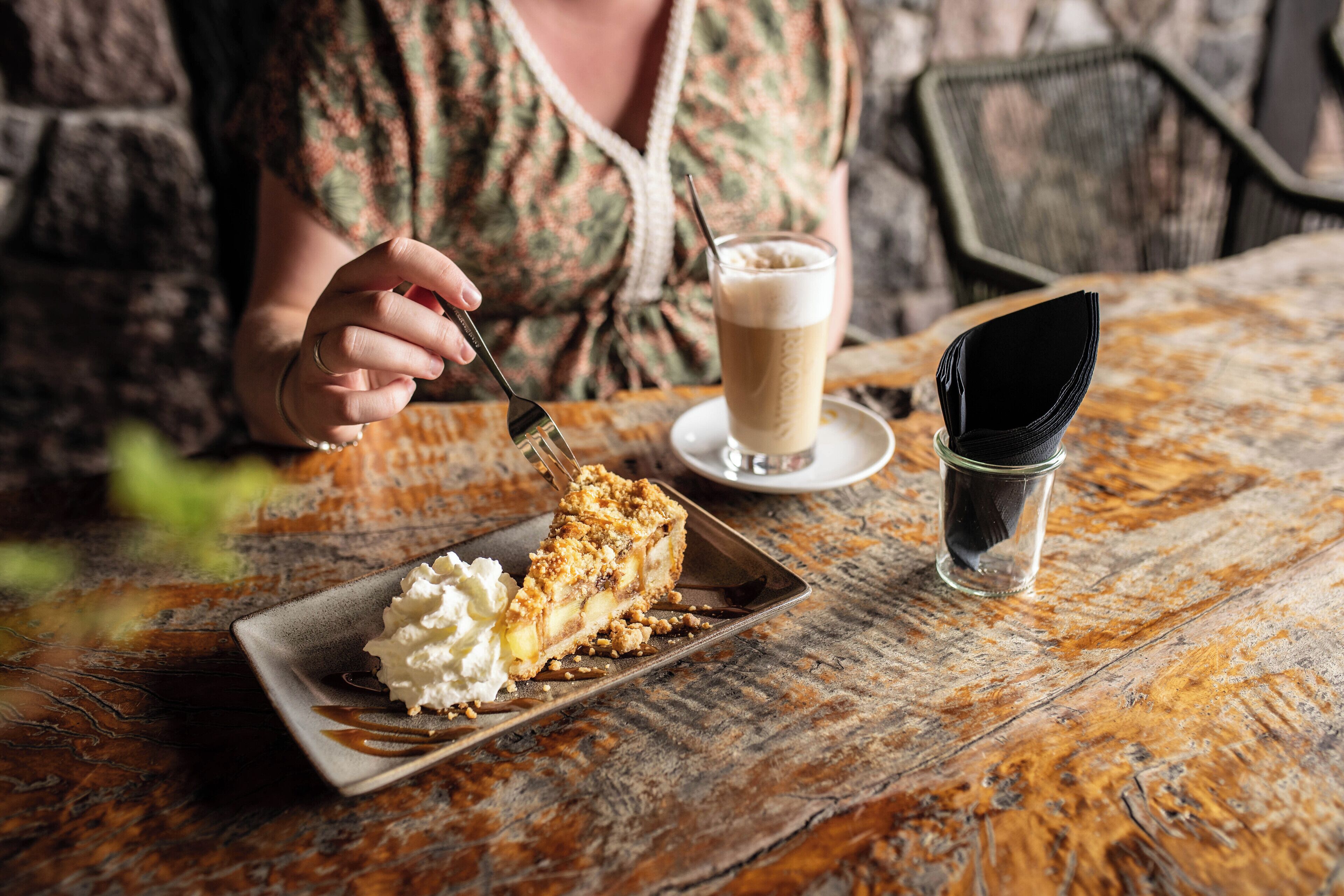 A slice of pie with whipped cream on a plate, a glass of coffee, and a napkin on a rustic wooden table.