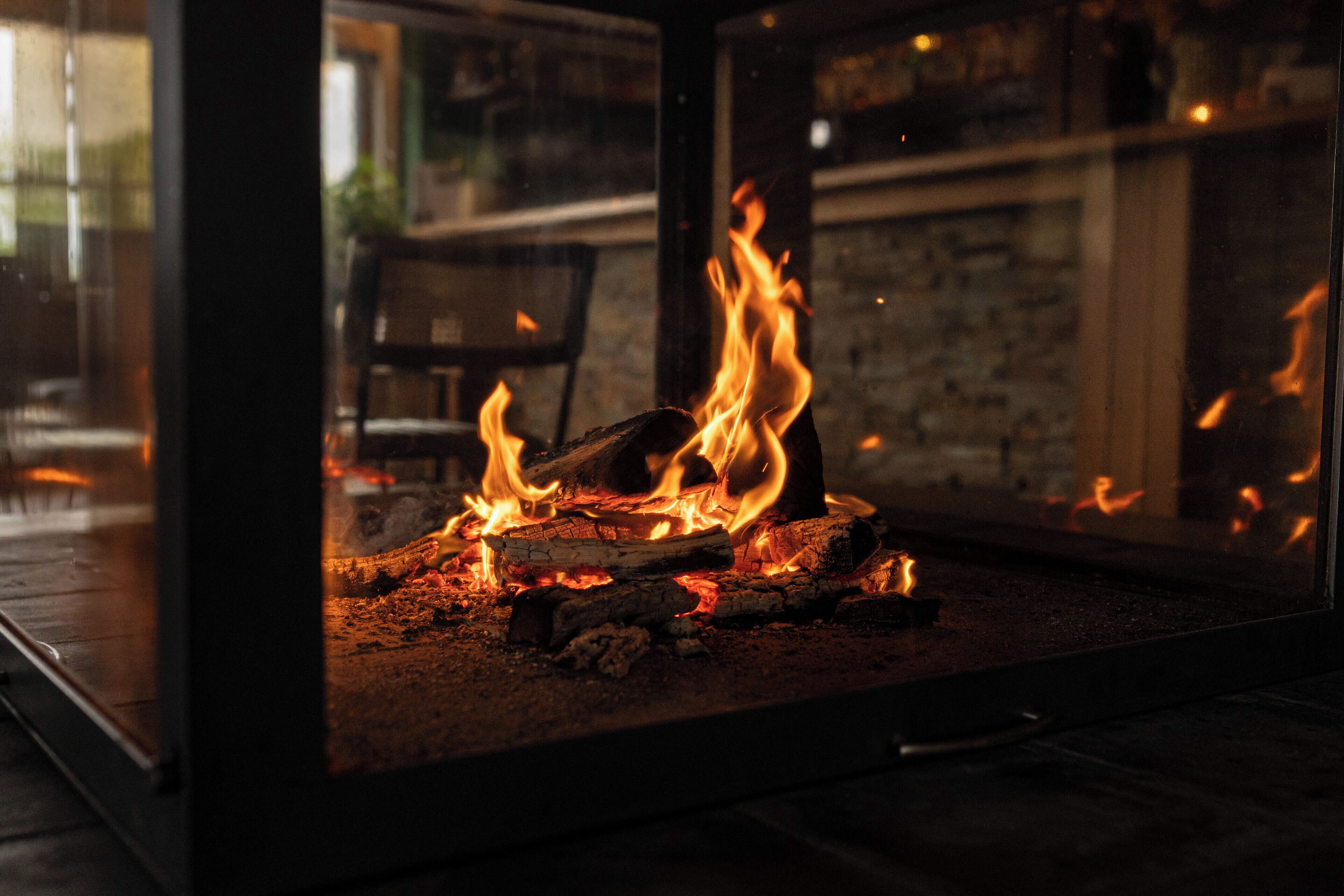 Una chimenea de vidrio con llamas visibles, una pared de piedra y una silla al fondo.
