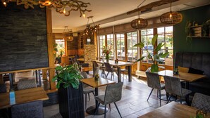 A restaurant interior with wooden tables, chairs, and hanging light fixtures. - Hotel Inn Salland (Raalte)