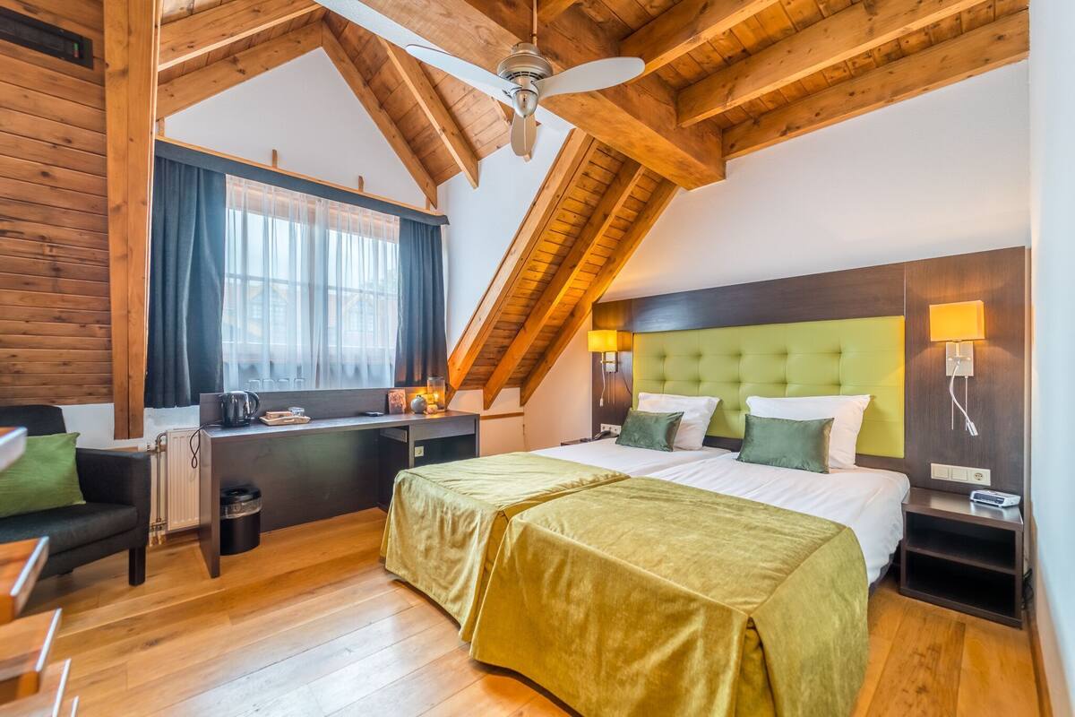 A room with a bed, a desk, a chair, a window with curtains, and a ceiling fan.