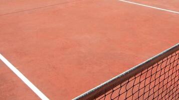 Una cancha de tenis con una red, rodeada de árboles y montañas al fondo.