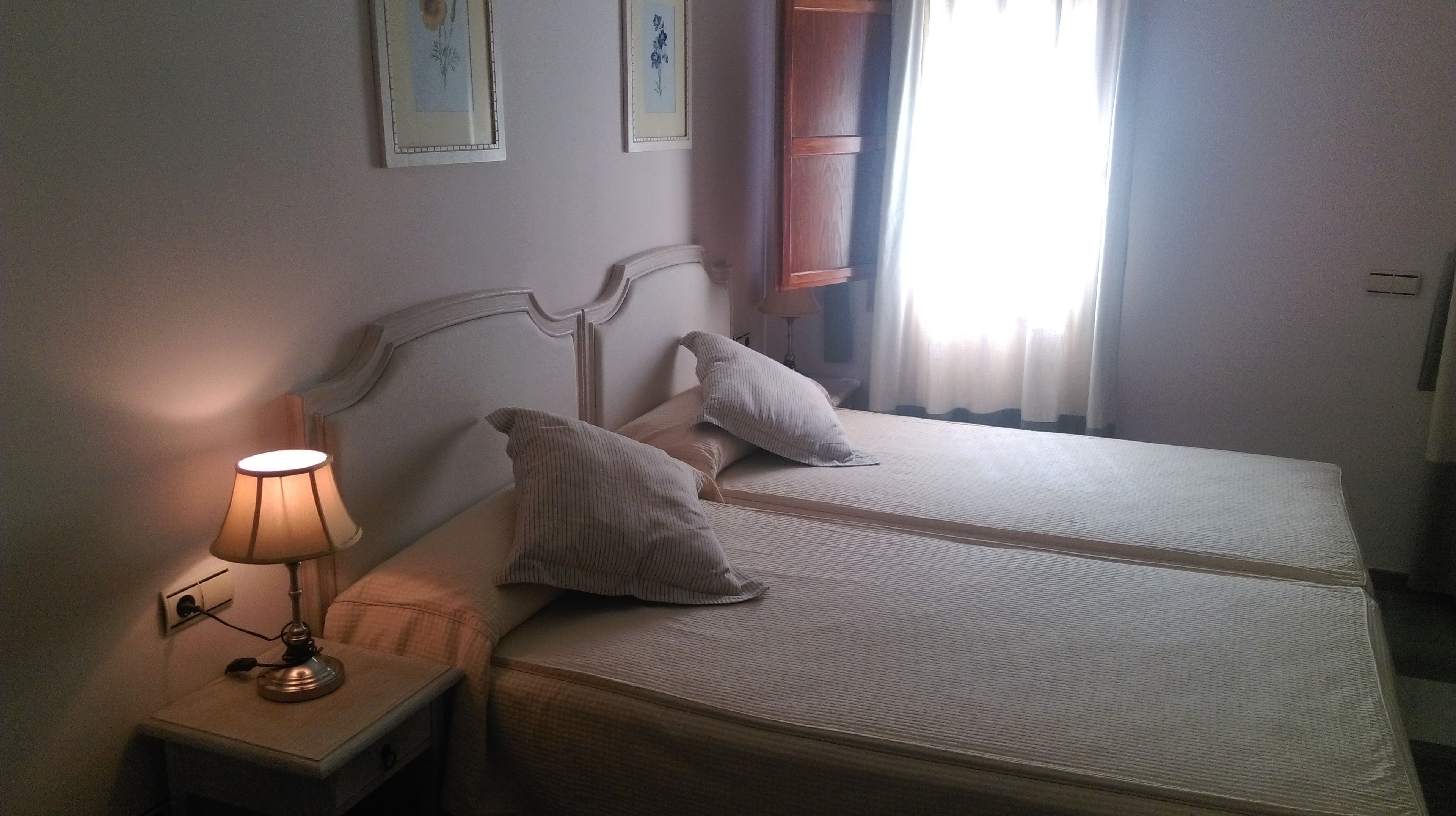A double bed with two pillows, a bedside lamp, and framed artwork on the wall.