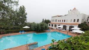 A swimming pool with lounge chairs and umbrellas, surrounded by greenery and a white building with arches. - Villa Turística de Laujar de Andarax (Laujar de Andarax)