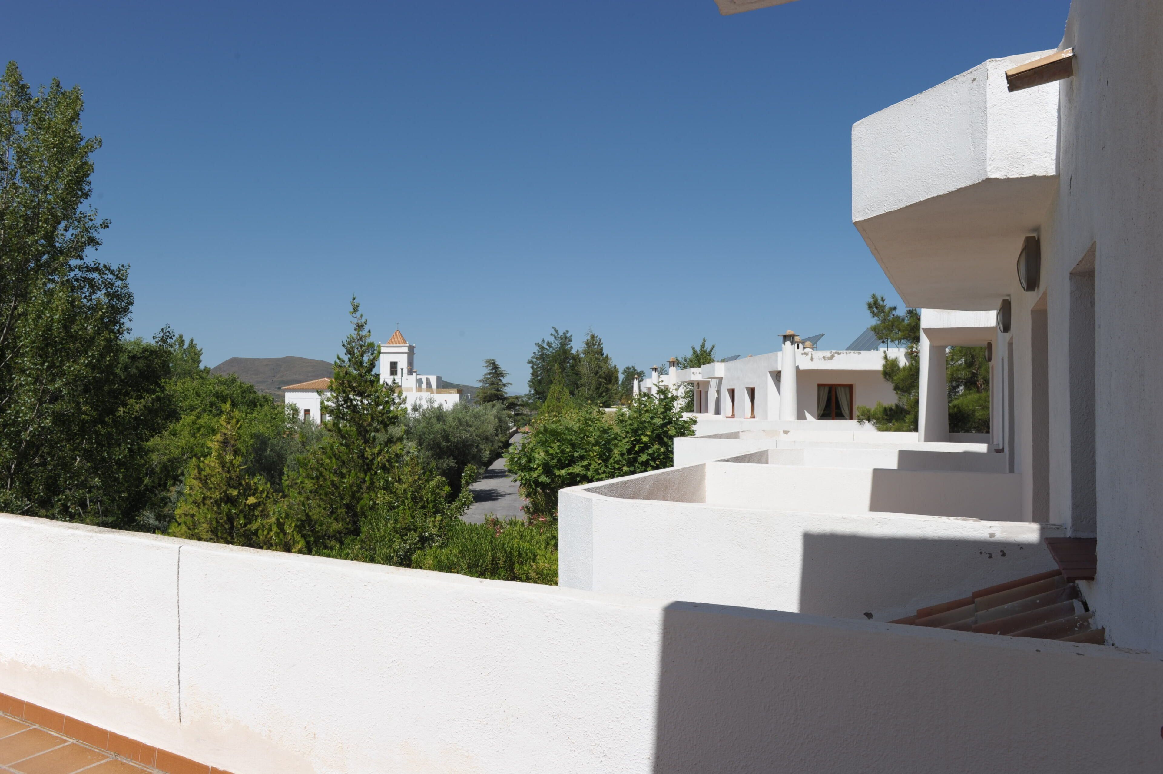 A white building with a balcony overlooking a clear blue sky and a distant mountain.