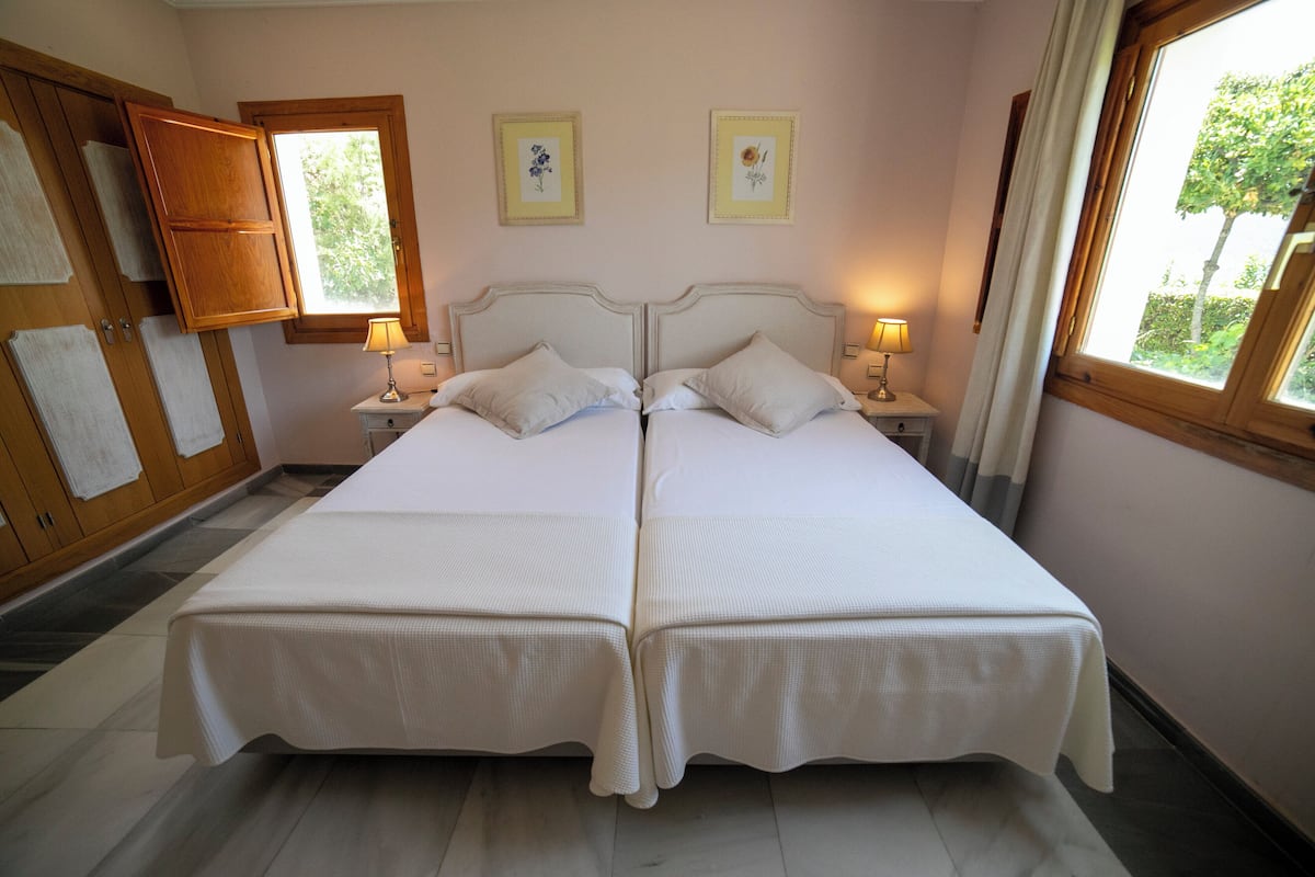 A double bed with white bedding, two bedside tables with lamps, a wooden wardrobe, and two framed pictures on the wall.