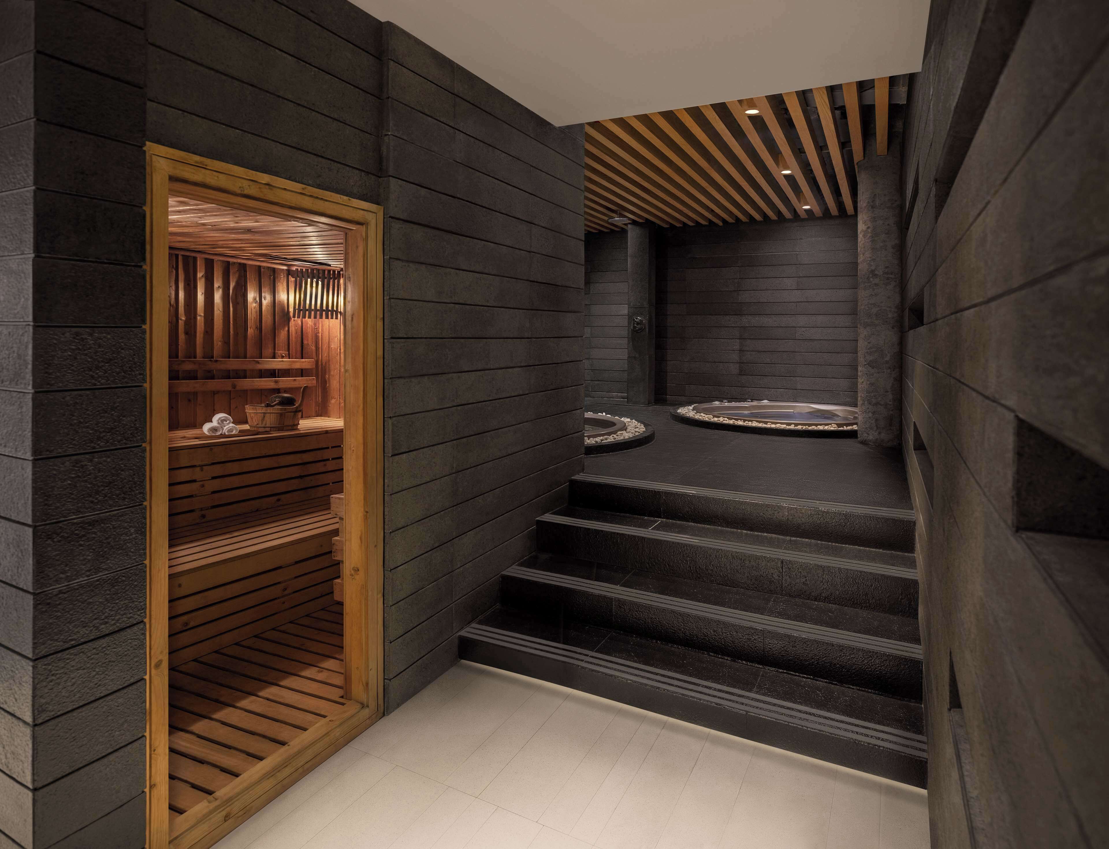 Un intérieur moderne avec des murs en pierre sombre, des escaliers en bois et un espace sauna équipé de bancs et de serviettes.