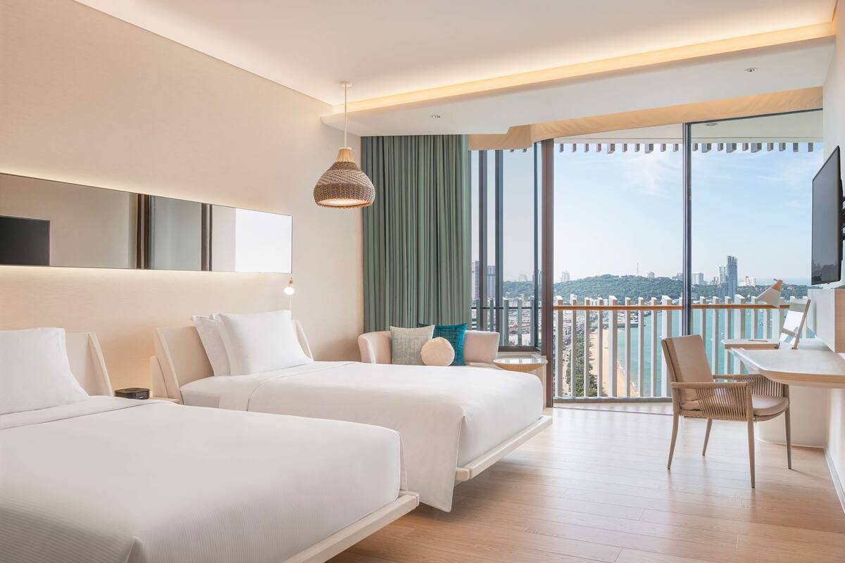 Ett modernt hotellrum med två sängar, ett skrivbord och utsikt över staden.