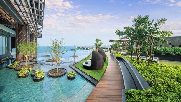 A modern resort with a swimming pool, wooden deck, and lush greenery. - Hilton Pattaya (Pattaya)