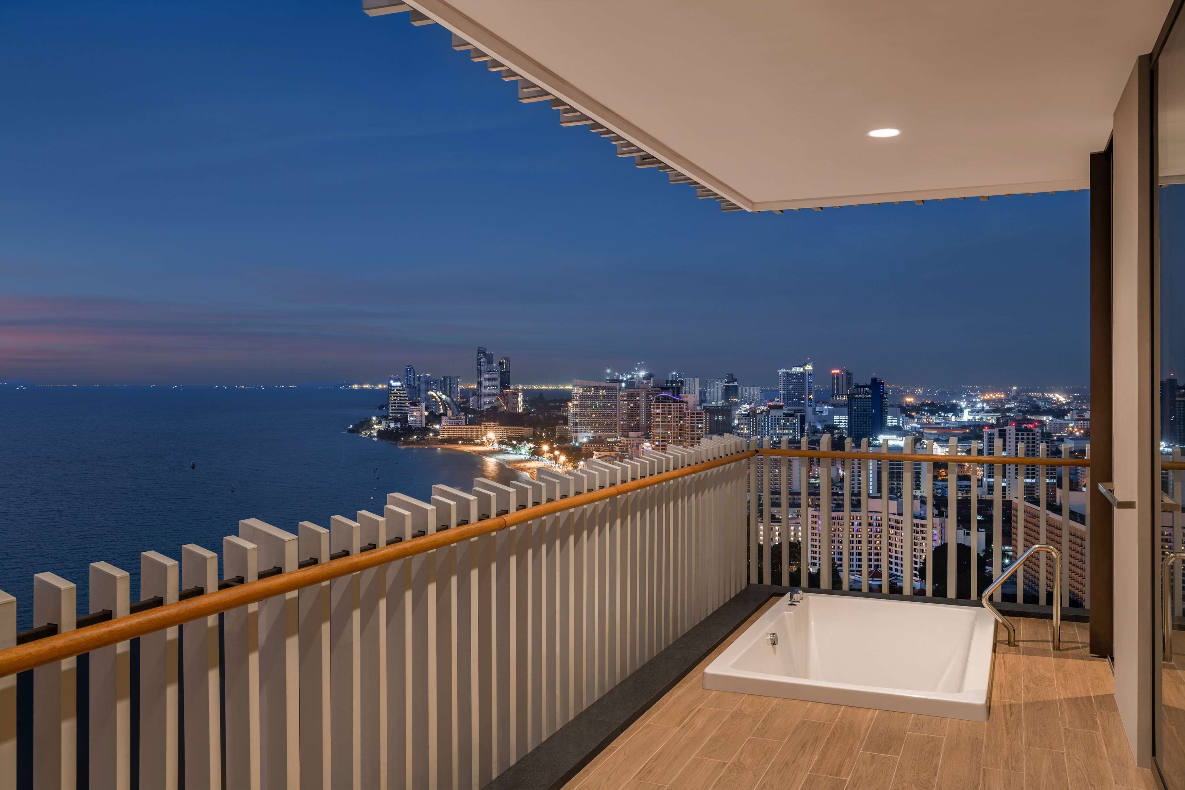 A balcony with a city view, a white bathtub, and a wooden railing.