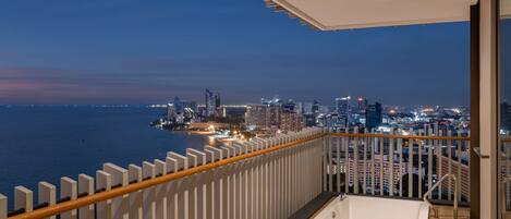 A balcony with a city view, a white bathtub, and a wooden railing.