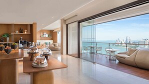 En moderne hotellobby med en træreception, et buffetområde og et siddeområde med udsigt over byen og havet.