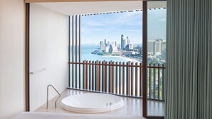 A modern bathroom with a large bathtub, a view of a city skyline, and a balcony with a railing. - Hilton Pattaya (Pattaya)