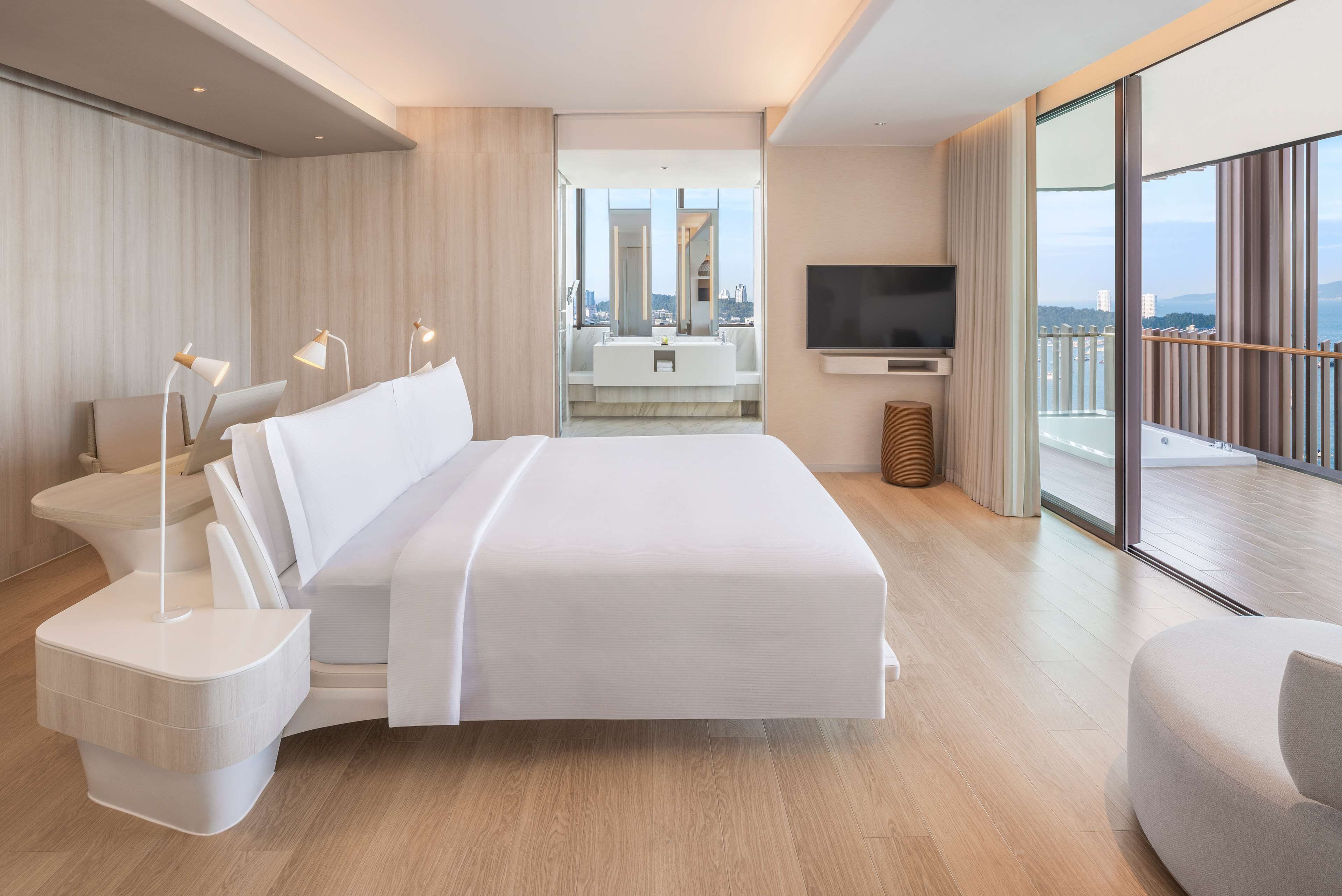 Habitació d'hotel moderna amb un llit gran, abacines, televisió i un balcó amb vista a la ciutat.