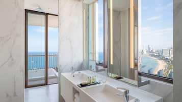A modern bathroom with a large mirror, two sinks, and a view of the ocean and cityscape.