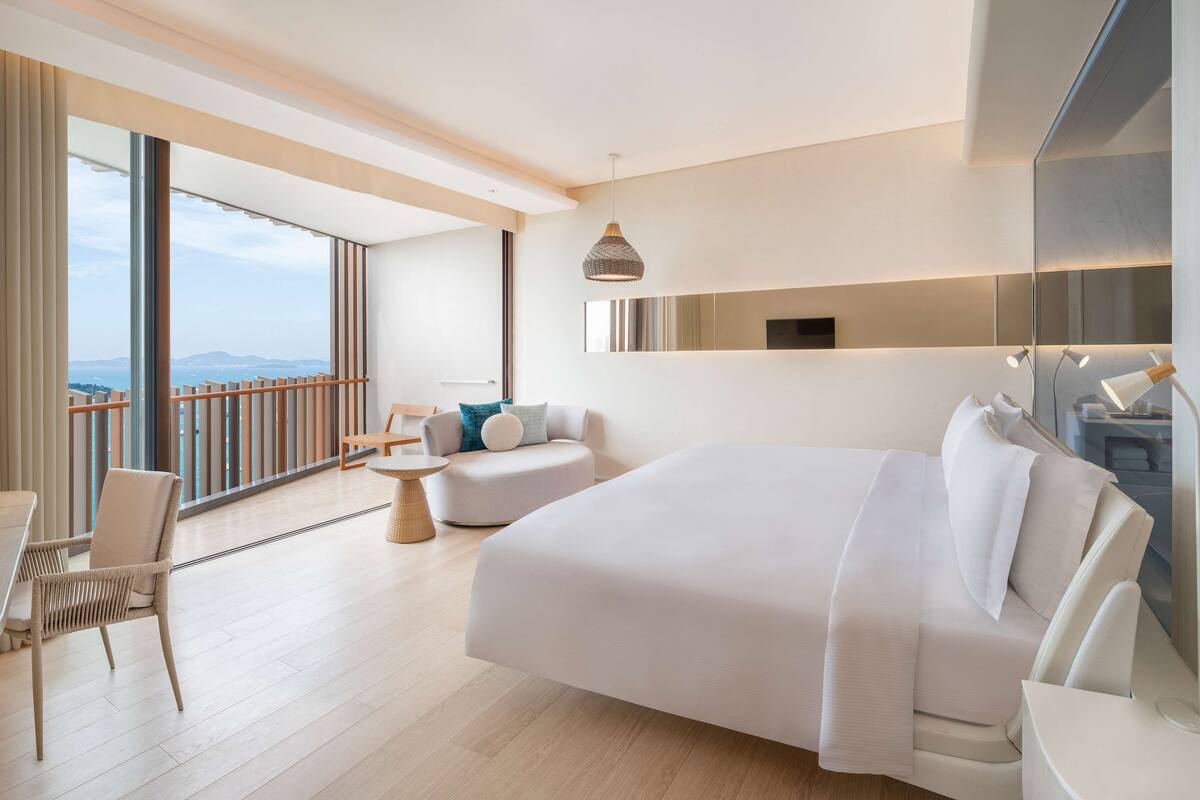 Ett modernt hotellrum med en stor säng, en sittgrupp med soffa och fåtöljer, ett litet bord och en balkong med ett räcke.
