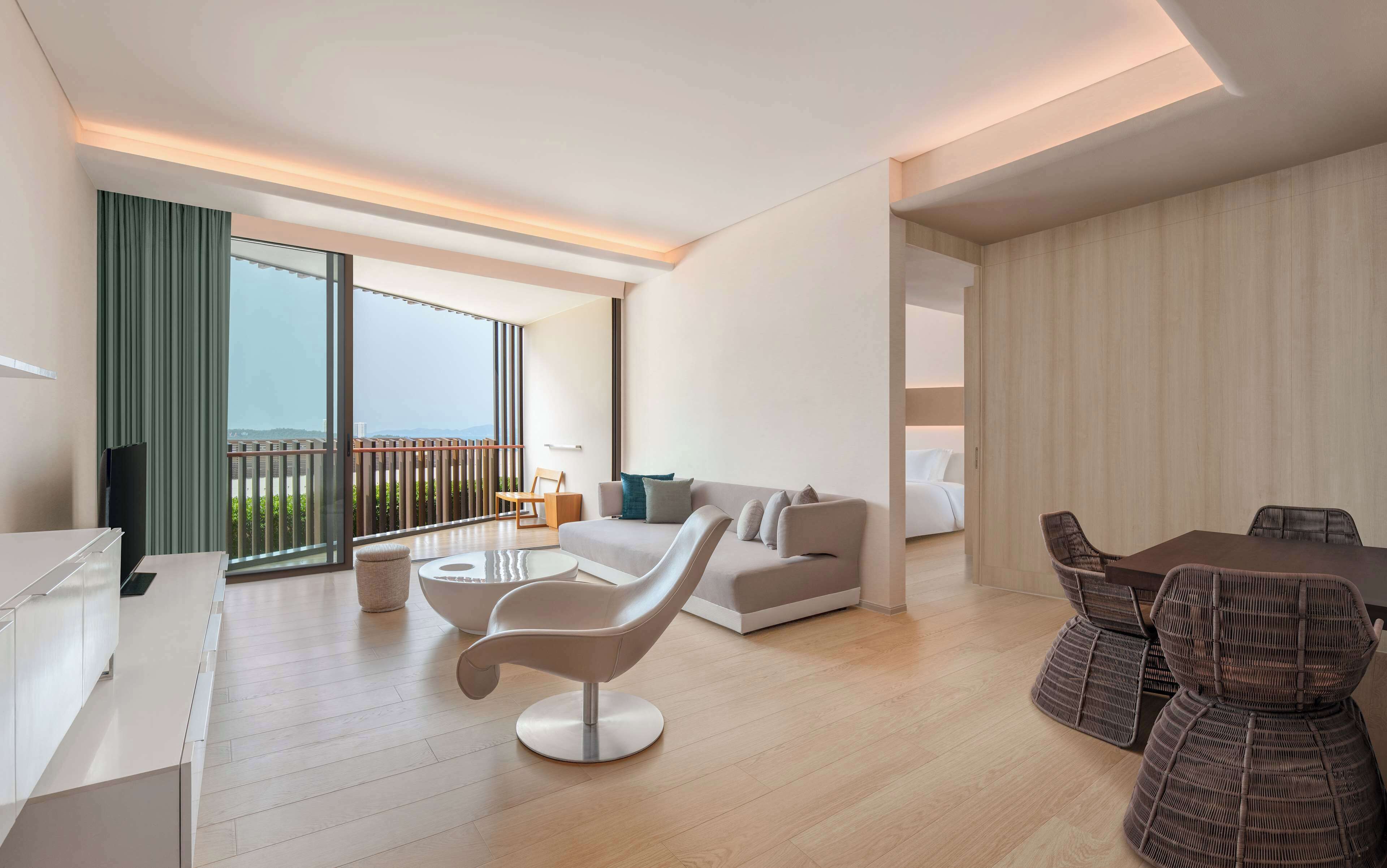 Una sala de estar moderna con un sofá, una silla blanca, una mesa de comedor con sillas y un balcón con vistas.