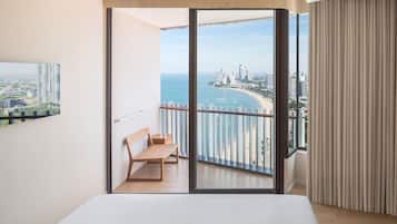 A modern bedroom with a balcony, a wooden bench, and a cityscape view.