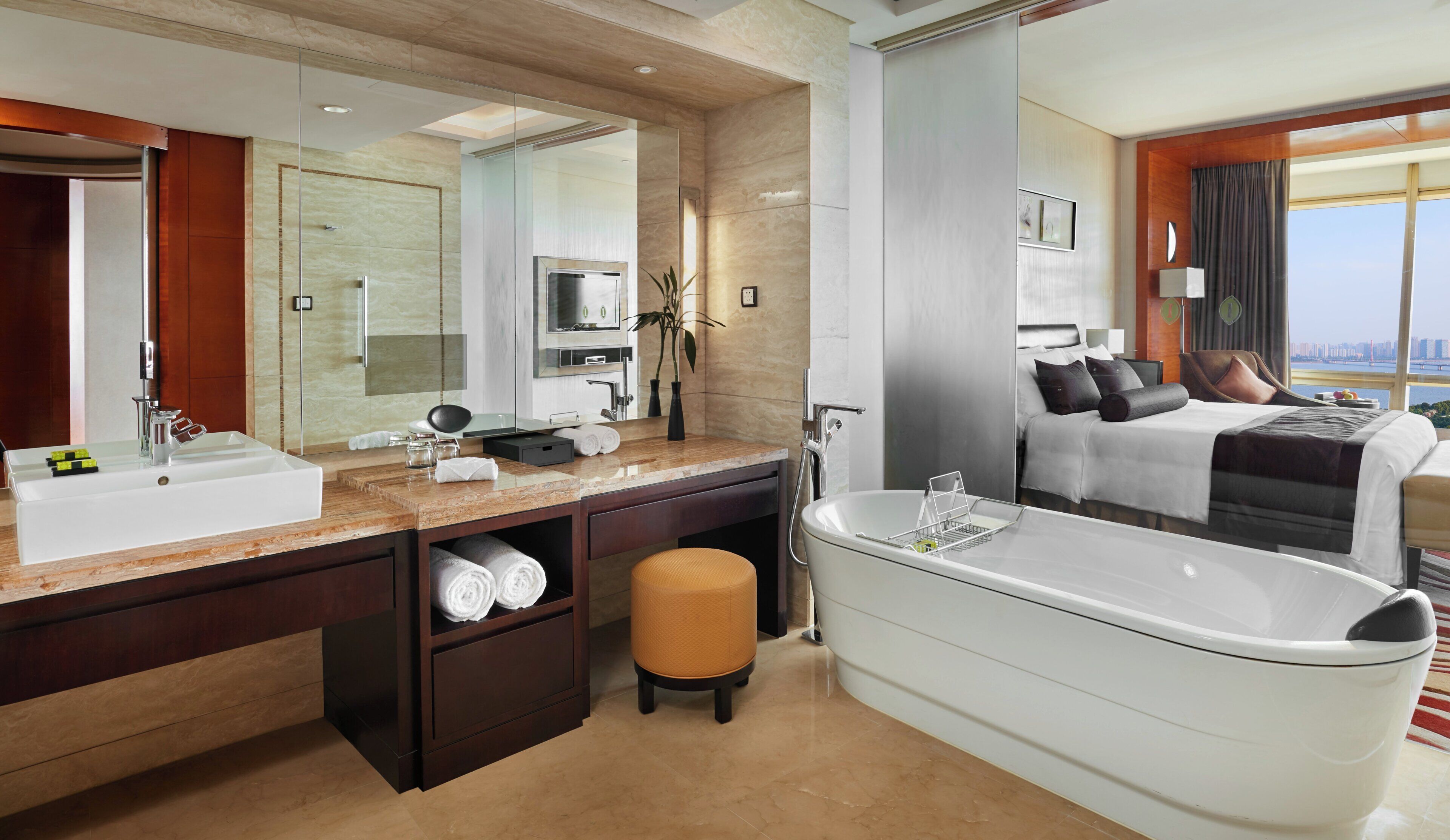 A modern bathroom with a large bathtub, a vanity with a mirror, and a view of a cityscape through a large window.