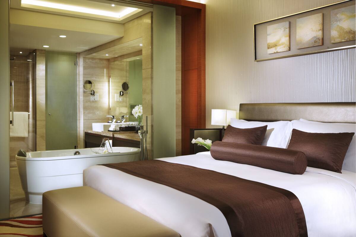 A hotel room with a large bed, a separate bathroom, and a view of the city.