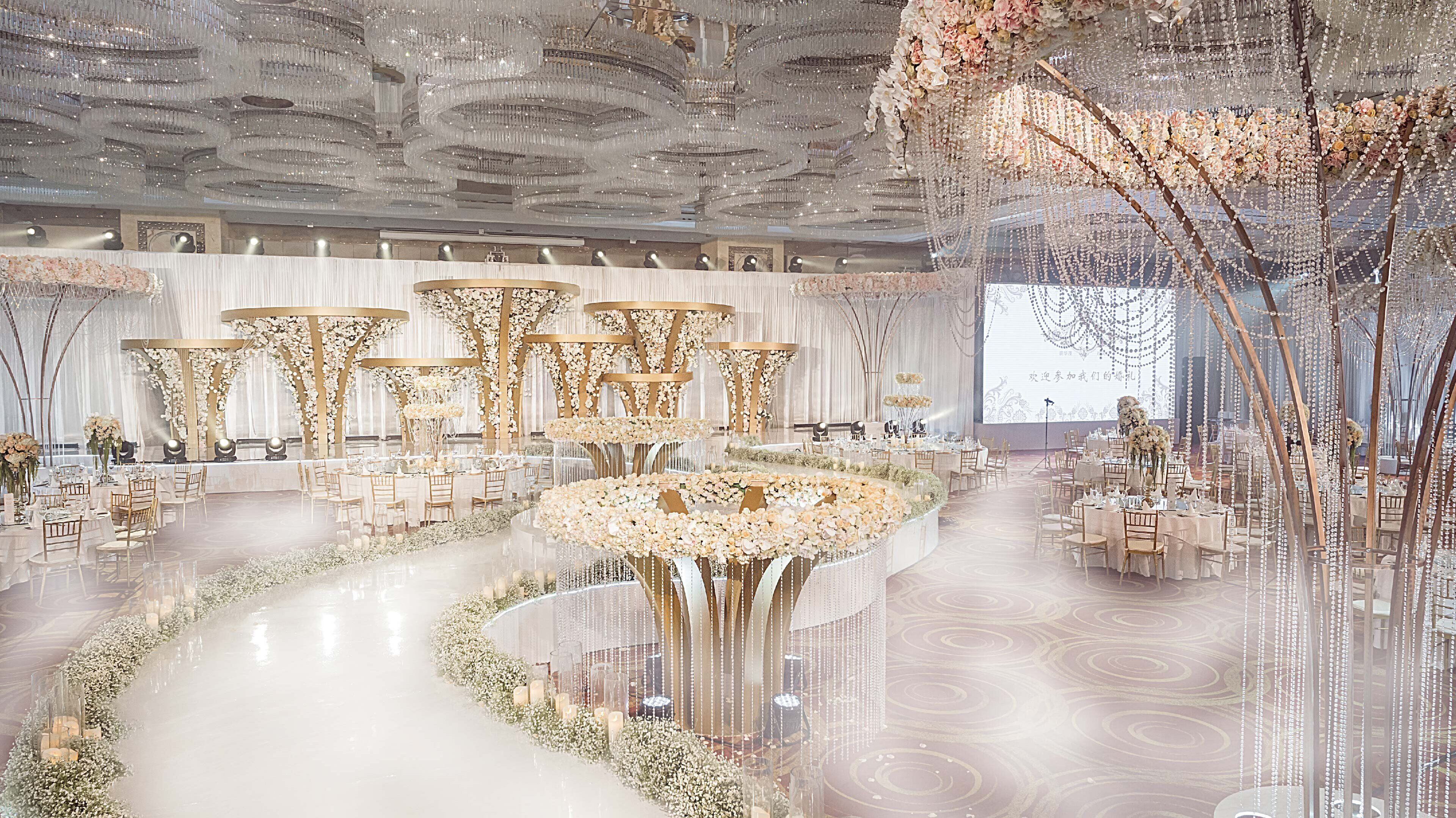 A grand hall with tiered seating, chandeliers, and floral arrangements.