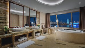 Un baño moderno con lavamanos dobles, un espejo grande, una bañera y vistas a un paisaje urbano nocturno.