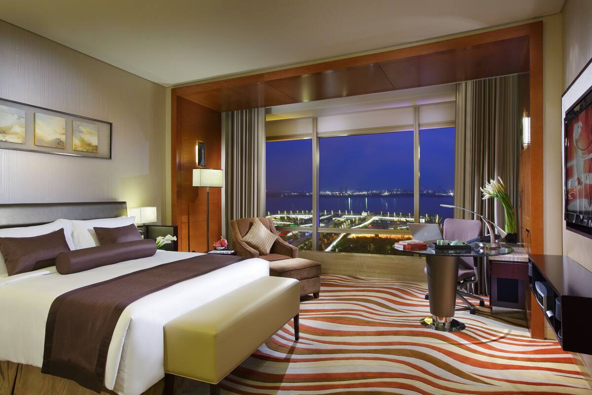 A hotel room with a large bed, a desk, and a view of the city at night.