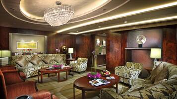 A hotel lobby with a chandelier, patterned sofas, a coffee table, and a dining area.