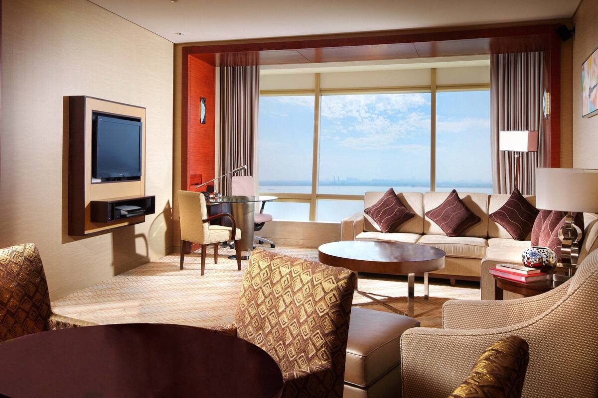 A hotel room with a large window, a television, a sofa, a coffee table, and a desk with a chair.