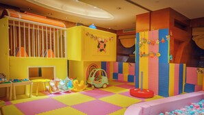 Un área de juegos interior muy colorida con una piscina de pelotas, estructuras para jugar y un suelo acolchado.