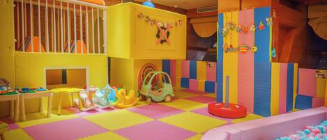 Un área de juegos interior muy colorida con una piscina de pelotas, estructuras para jugar y un suelo acolchado.